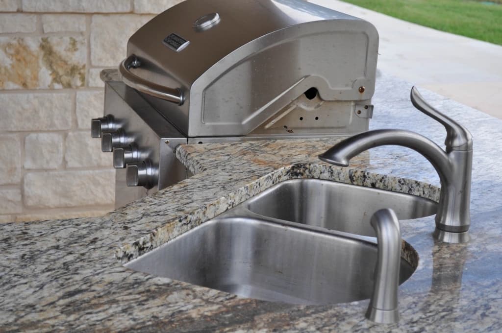 The casita's outdoor kitchen, built-in stainless grill and double sink set in granite, limestone wall behind