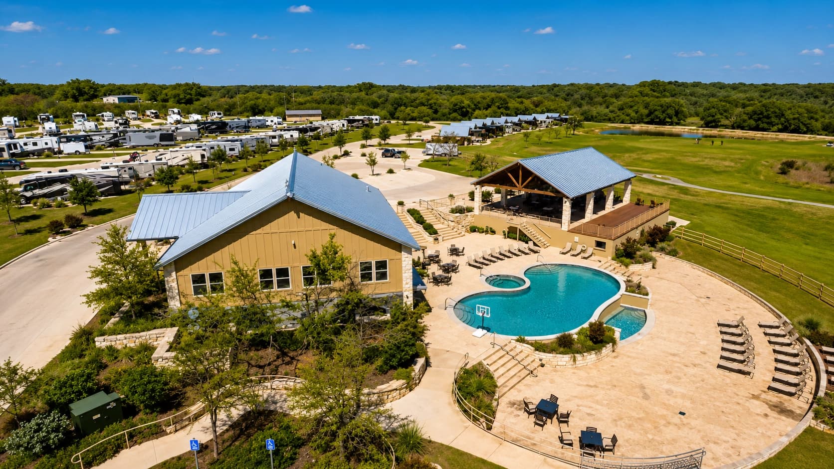 Aerial view of the resort grounds in full summer — the pool, hot tub, and pavilion beside the clubhouse